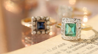 Two Carrie Elizabeth vintage rings on a vintage book - emerald and sapphire cluster rings, with diamonds 
